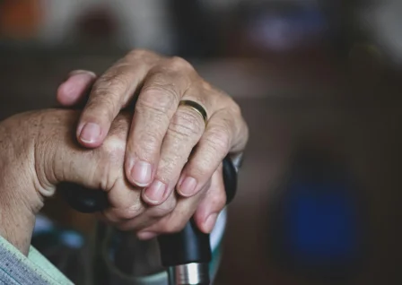 Elderly person's hands resting on a walking stick, symbolising aged care and support services