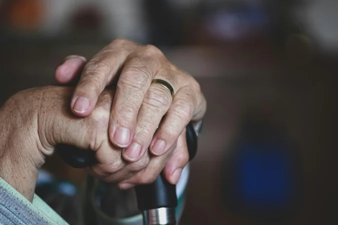 Elderly person's hands resting on a walking stick, symbolising aged care and support services