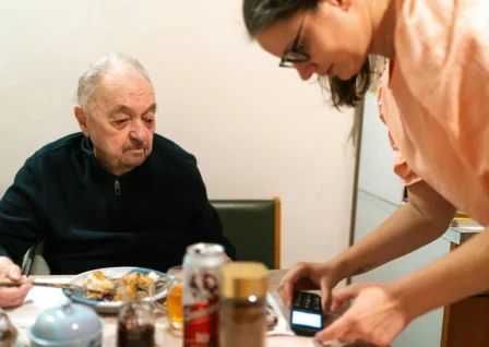 Carer assisting elderly man with digital payment during mealtime at home