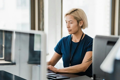 A focused aged care software developer with short blonde hair working at a desktop computer in a bright modern office.