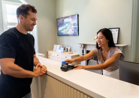 Healthcare receptionist processing a card payment on an EFTPOS terminal for a patient at a clinic reception