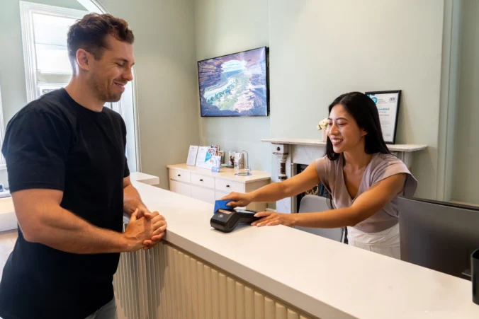 Healthcare receptionist processing a card payment on an EFTPOS terminal for a patient at a clinic reception